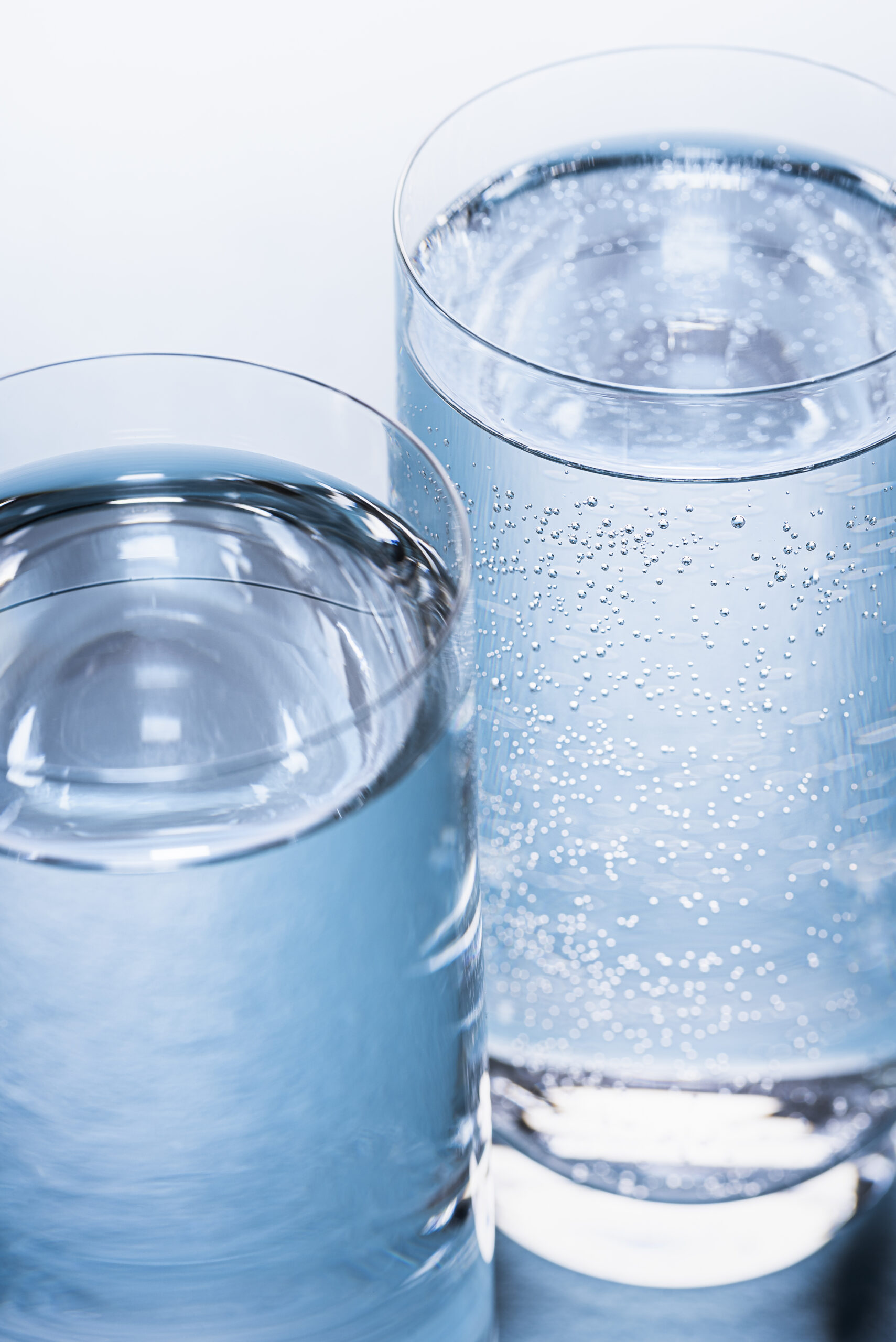 Close-up of glasses with mineral and tonic water on a blue table. Mineral water and tonic water glasses in natural light on a blue background.